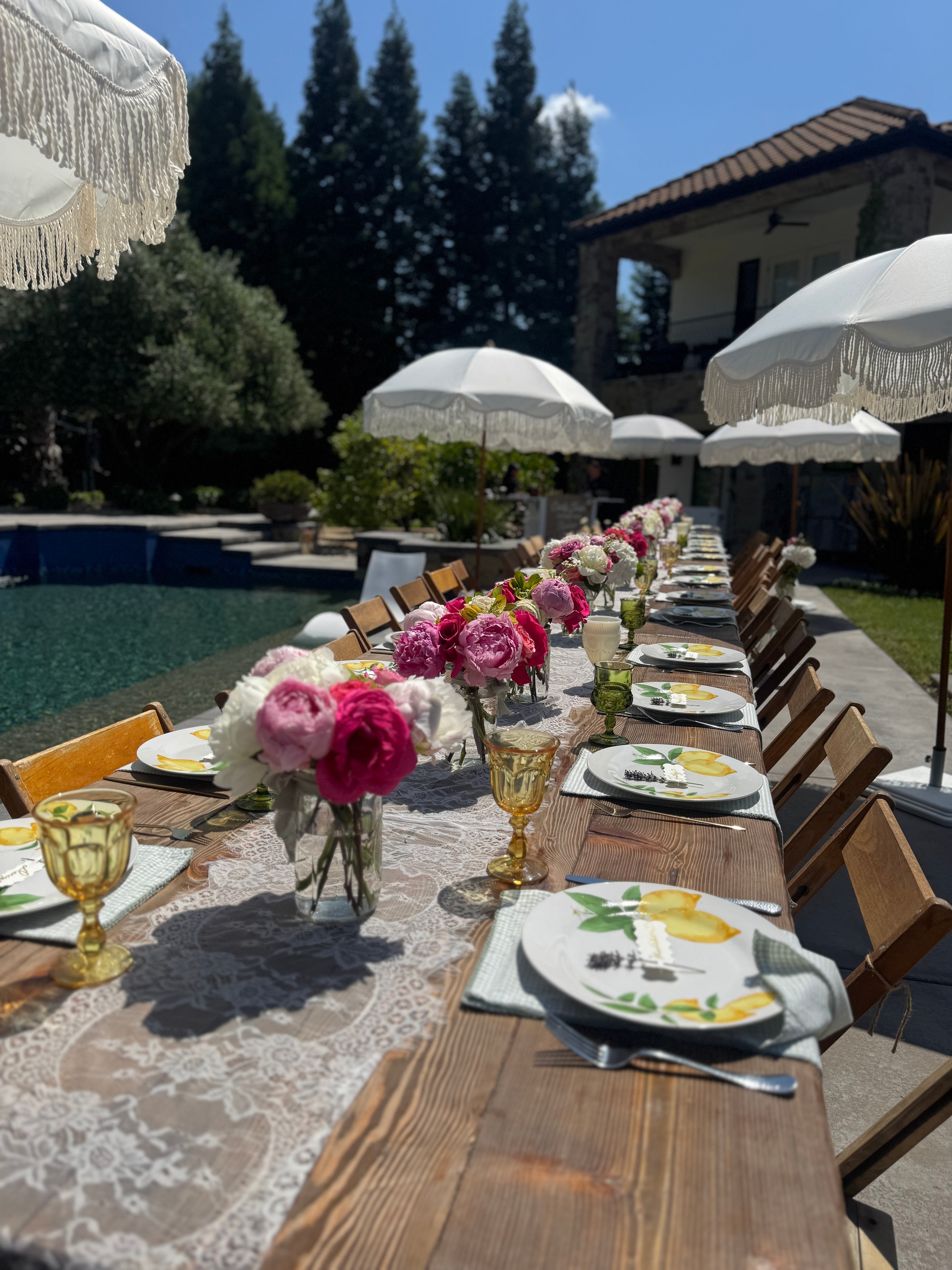 Poolside farm table with pink peonies and fringe umbrellas