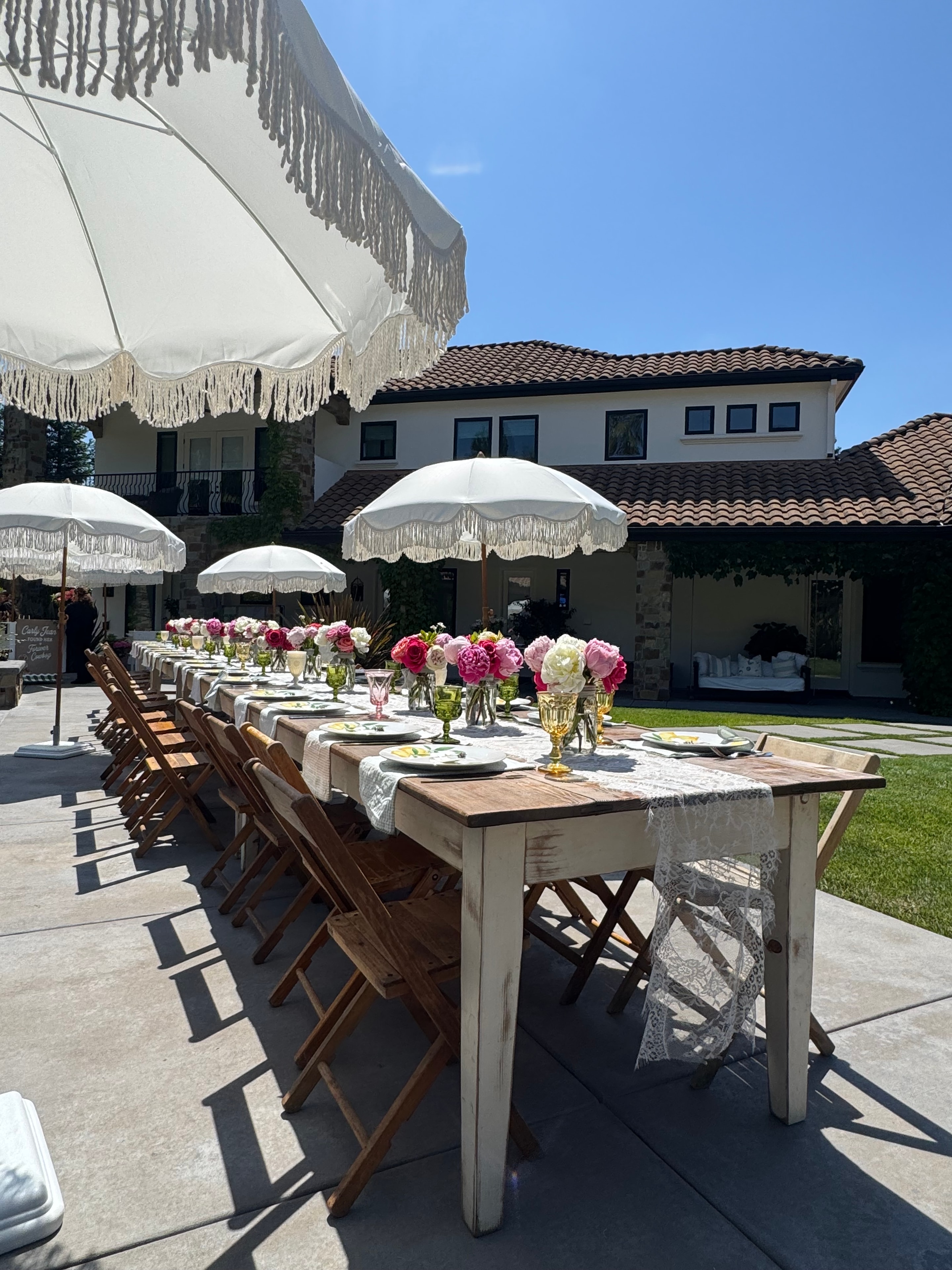 Wide outdoor poolside table setup with fringe umbrellas